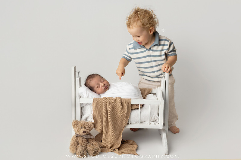 Big brother smiling beside his newborn baby brother during a sibling newborn photography session.