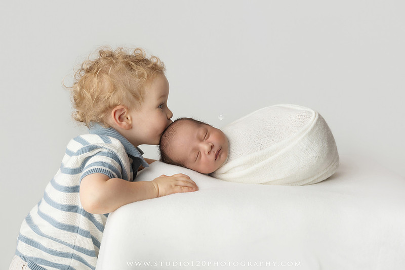 Big brother smiling beside his newborn baby brother during a sibling newborn photography session.