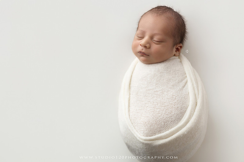 Big brother smiling beside his newborn baby brother during a sibling newborn photography session.