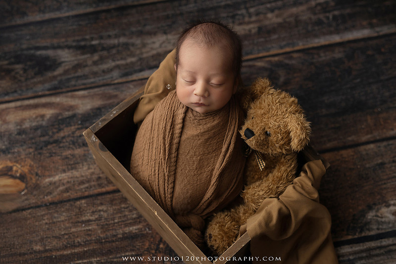 Big brother smiling beside his newborn baby brother during a sibling newborn photography session.