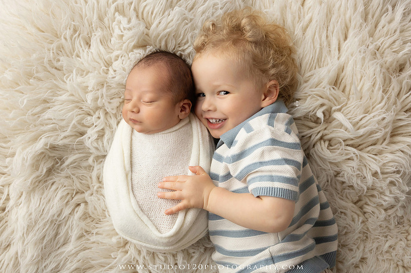 Big brother smiling beside his newborn baby brother during a sibling newborn photography session.