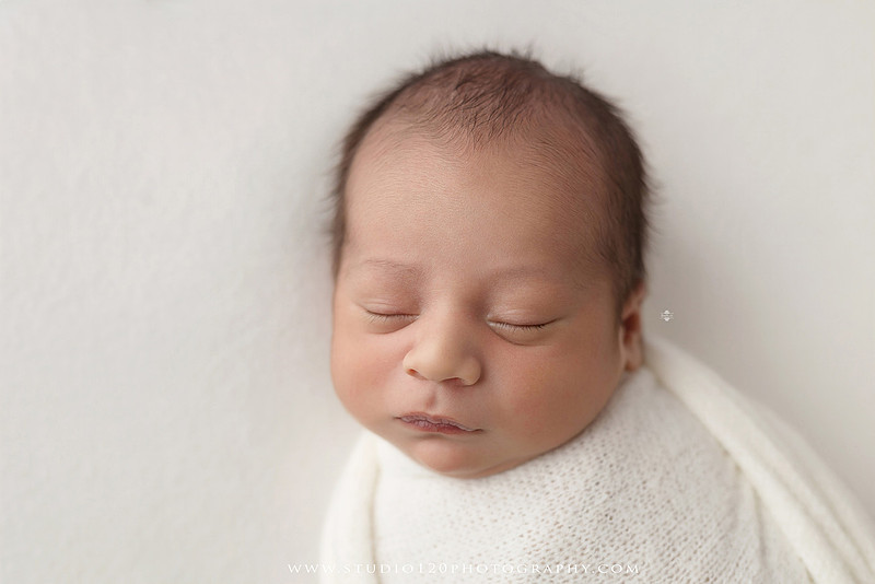 Big brother smiling beside his newborn baby brother during a sibling newborn photography session.