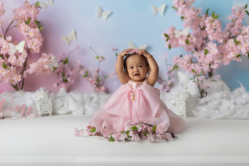 One-year-old girl enjoying an elegant blush pink floral cake smash with cherry blossoms, butterflies, and a custom birthday cake during a luxury first birthday photography session at Studio 120 Photography in Ramona, California.