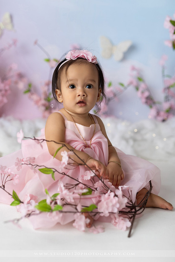 One-year-old girl enjoying an elegant blush pink floral cake smash with cherry blossoms, butterflies, and a custom birthday cake during a luxury first birthday photography session at Studio 120 Photography in Ramona, California.