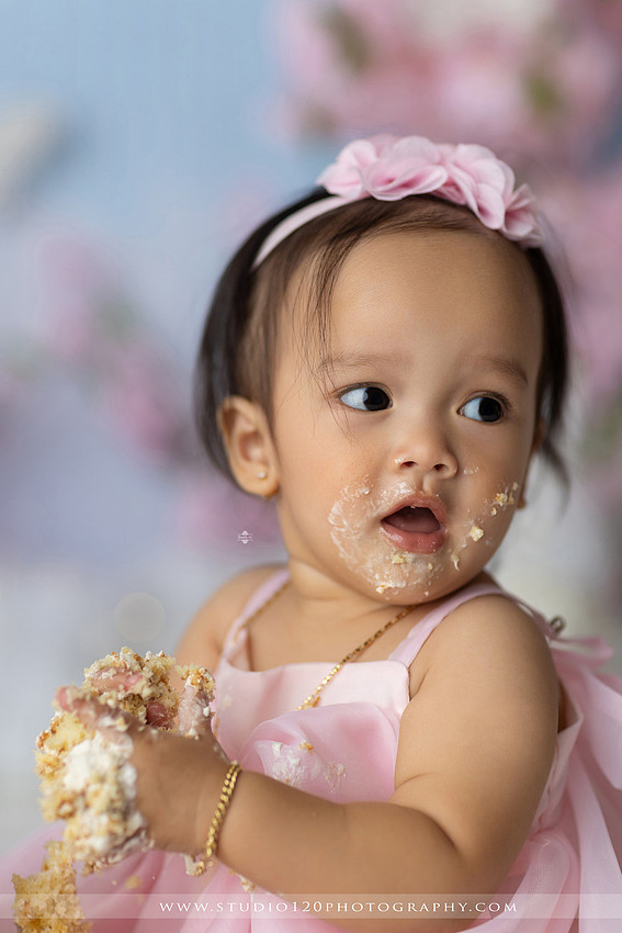 One-year-old girl enjoying an elegant blush pink floral cake smash with cherry blossoms, butterflies, and a custom birthday cake during a luxury first birthday photography session at Studio 120 Photography in Ramona, California.