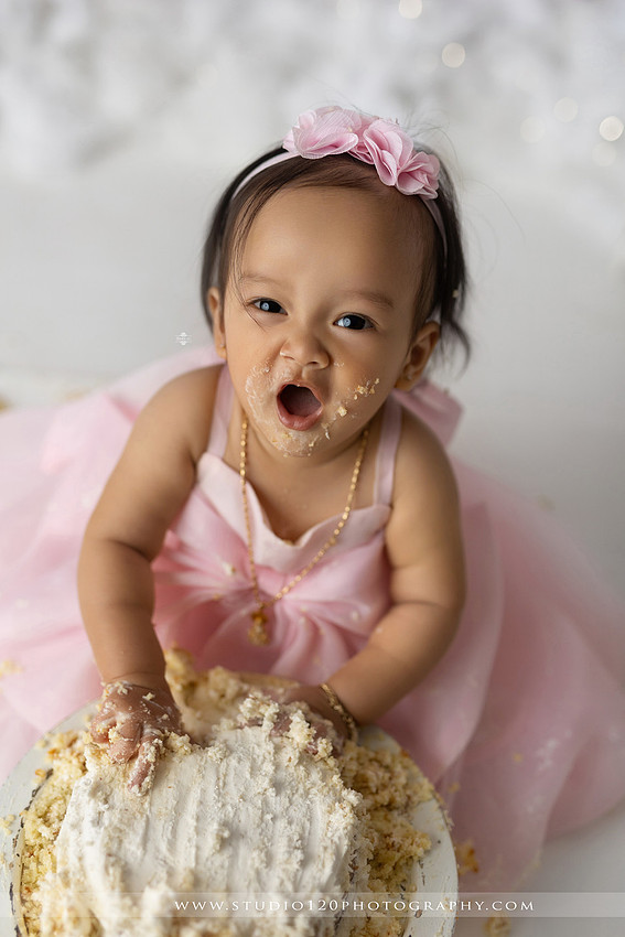 One-year-old girl enjoying an elegant blush pink floral cake smash with cherry blossoms, butterflies, and a custom birthday cake during a luxury first birthday photography session at Studio 120 Photography in Ramona, California.