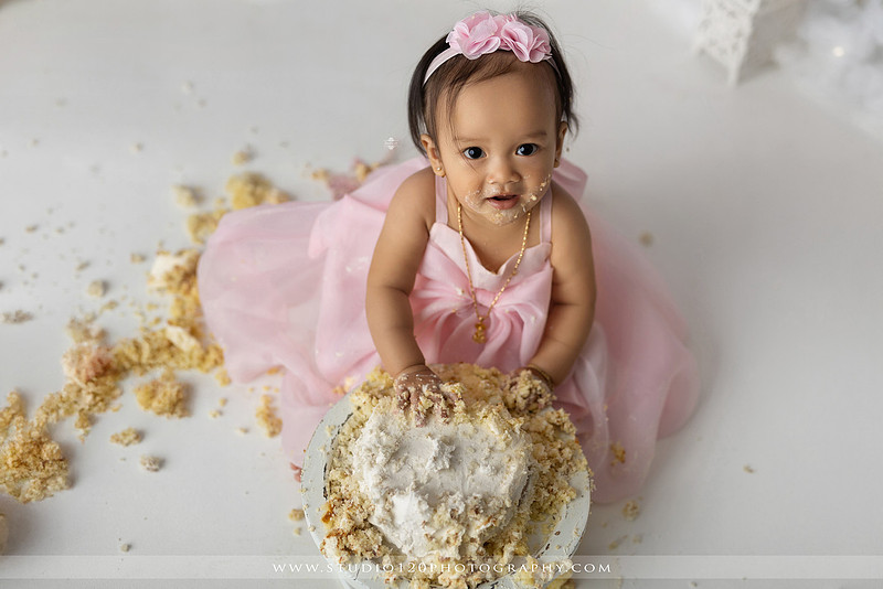One-year-old girl enjoying an elegant blush pink floral cake smash with cherry blossoms, butterflies, and a custom birthday cake during a luxury first birthday photography session at Studio 120 Photography in Ramona, California.