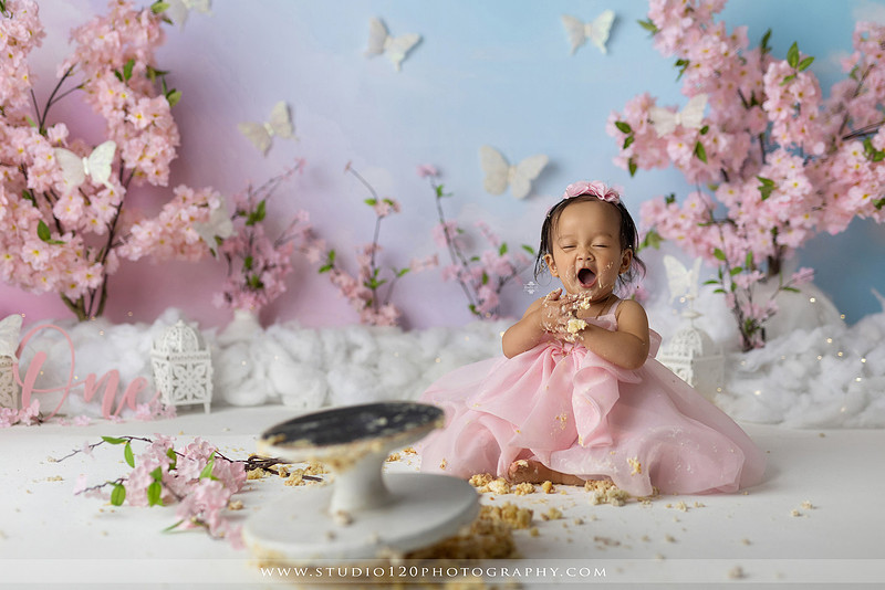 One-year-old girl enjoying an elegant blush pink floral cake smash with cherry blossoms, butterflies, and a custom birthday cake during a luxury first birthday photography session at Studio 120 Photography in Ramona, California.