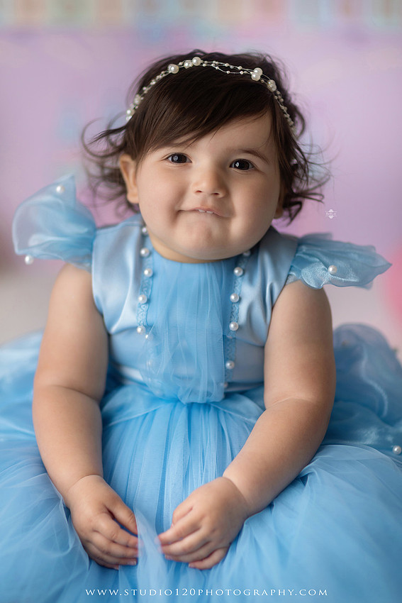 Disneyland-inspired first birthday cake smash featuring a baby girl in a blue princess dress with pastel balloons, whimsical amusement park décor, custom birthday backdrop, milestone portraits, and cake smash photography by Studio 120 Photography in Ramona, serving San Diego County.