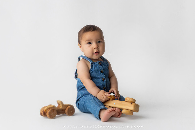 Baby boy sitter milestone portraits in Ramona photography studio featuring classic wooden toys, teddy bears, a vintage wooden bed, neutral props, natural textures, and timeless baby milestone photography capturing smiles, curiosity, and playful expressions.