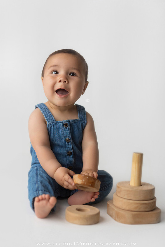 Baby boy sitter milestone portraits in Ramona photography studio featuring classic wooden toys, teddy bears, a vintage wooden bed, neutral props, natural textures, and timeless baby milestone photography capturing smiles, curiosity, and playful expressions.