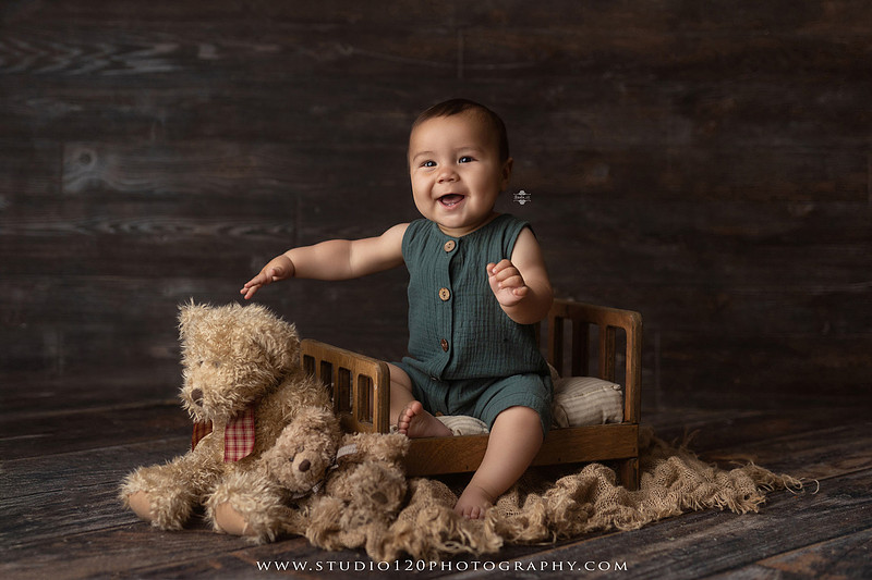 Baby boy sitter milestone portraits in Ramona photography studio featuring classic wooden toys, teddy bears, a vintage wooden bed, neutral props, natural textures, and timeless baby milestone photography capturing smiles, curiosity, and playful expressions.