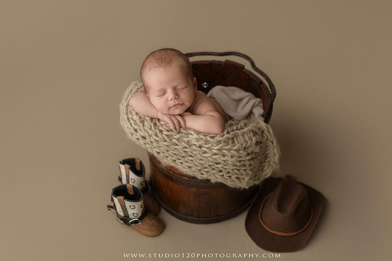 Professional newborn photography session featuring a sleeping baby boy in rustic western-inspired setups with cowboy hats, neutral wraps, wooden props, greenery, and vintage accents, along with heartfelt family portraits with parents and their dogs at Studio 120 Photography in Ramona, California.