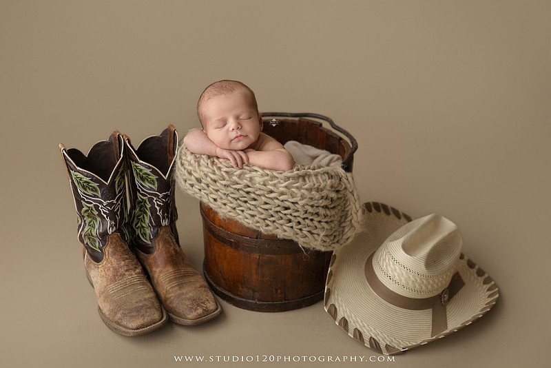 Professional newborn photography session featuring a sleeping baby boy in rustic western-inspired setups with cowboy hats, neutral wraps, wooden props, greenery, and vintage accents, along with heartfelt family portraits with parents and their dogs at Studio 120 Photography in Ramona, California.