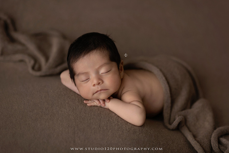Newborn baby boy sleeping peacefully in neutral-toned wraps and rustic props, including a wooden bucket, teddy bear, and western-inspired cowboy outfit with denim overalls and a cowboy hat during a custom newborn photography session at Studio 120 Photography in Ramona, California.