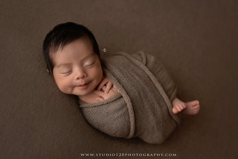 Newborn baby boy sleeping peacefully in neutral-toned wraps and rustic props, including a wooden bucket, teddy bear, and western-inspired cowboy outfit with denim overalls and a cowboy hat during a custom newborn photography session at Studio 120 Photography in Ramona, California.