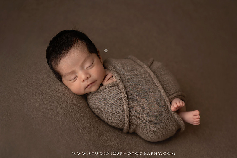 Newborn baby boy sleeping peacefully in neutral-toned wraps and rustic props, including a wooden bucket, teddy bear, and western-inspired cowboy outfit with denim overalls and a cowboy hat during a custom newborn photography session at Studio 120 Photography in Ramona, California.