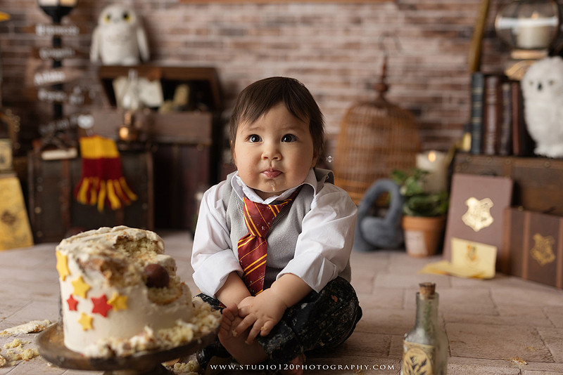 One-year-old boy dressed as a wizard smiling beside a Harry Potter-inspired birthday cake during a magical first birthday cake smash in San Diego.