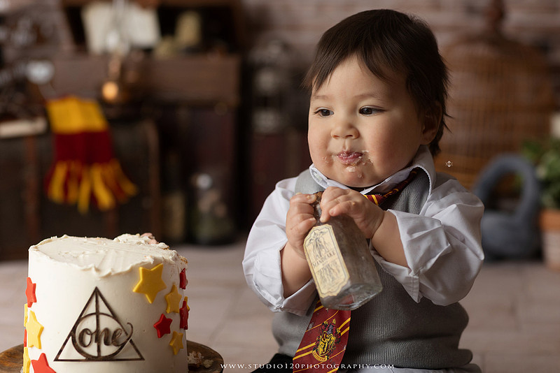One-year-old boy dressed as a wizard smiling beside a Harry Potter-inspired birthday cake during a magical first birthday cake smash in San Diego.