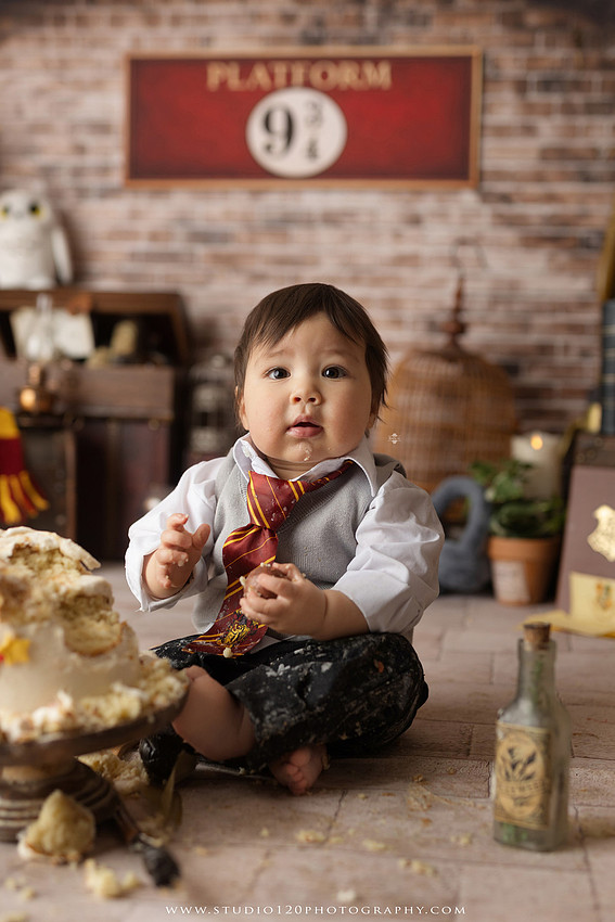 One-year-old boy dressed as a wizard smiling beside a Harry Potter-inspired birthday cake during a magical first birthday cake smash in San Diego.