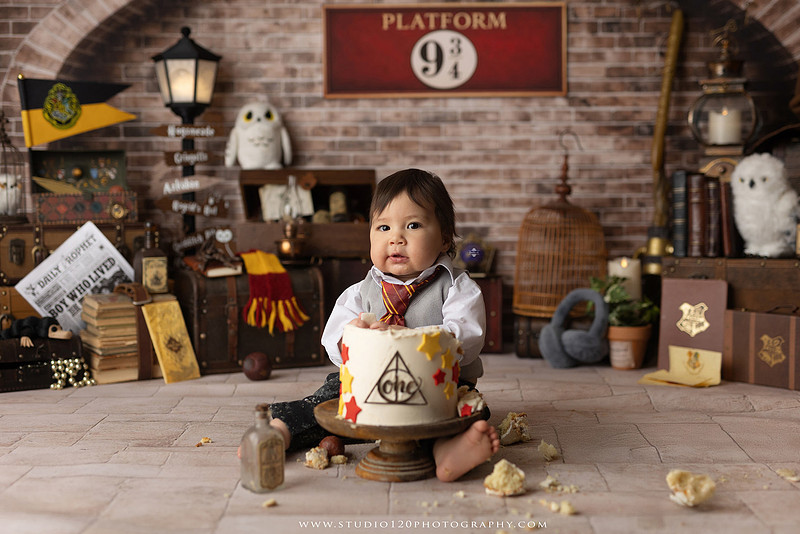 One-year-old boy dressed as a wizard smiling beside a Harry Potter-inspired birthday cake during a magical first birthday cake smash in San Diego.
