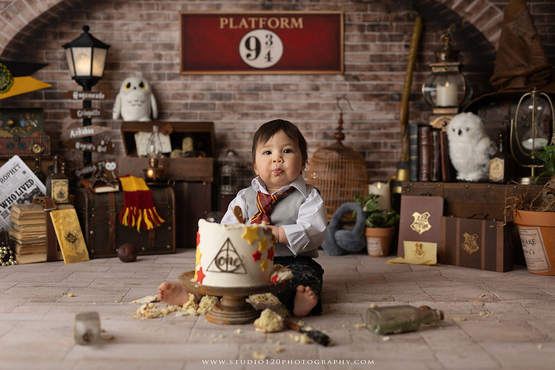 One-year-old boy dressed as a wizard smiling beside a Harry Potter-inspired birthday cake during a magical first birthday cake smash in San Diego.