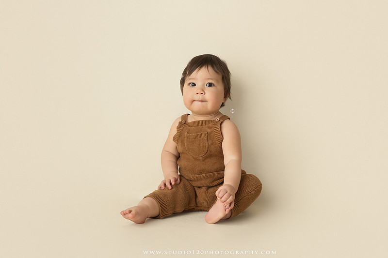Smiling one-year-old boy in a knit romper sitting on a wooden stool during a milestone portrait session at Studio 120 Photography in Ramona, California.