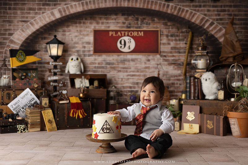 One-year-old boy dressed as a wizard smiling beside a Harry Potter-inspired birthday cake during a magical first birthday cake smash in San Diego.