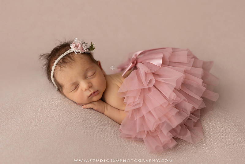 A collection of professional newborn portraits featuring a sleeping baby girl photographed in soft blush pink, ivory, and warm neutral tones. The gallery includes delicate floral headbands, a layered pink tutu, cozy cream wraps, a knitted lamb bonnet in a rustic wooden bucket, and beautiful cherry blossom accents. Images showcase a variety of classic newborn poses on textured blankets, nestled in a floral basket, and wrapped in timeless knit fabrics. Captured at Studio 120 Photography in Ramona, serving San Diego families with fine art newborn photography.