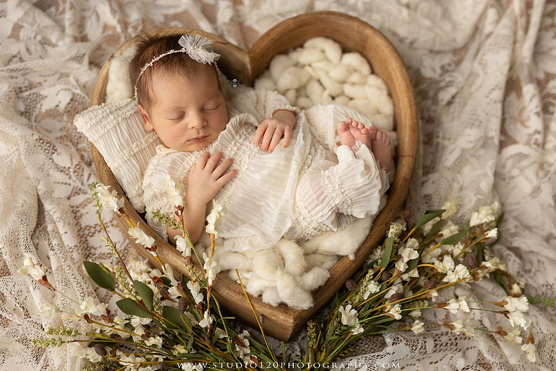 A collection of professional newborn portraits featuring a sleeping baby girl photographed in soft blush pink, ivory, and warm neutral tones. The gallery includes delicate floral headbands, a layered pink tutu, cozy cream wraps, a knitted lamb bonnet in a rustic wooden bucket, and beautiful cherry blossom accents. Images showcase a variety of classic newborn poses on textured blankets, nestled in a floral basket, and wrapped in timeless knit fabrics. Captured at Studio 120 Photography in Ramona, serving San Diego families with fine art newborn photography.