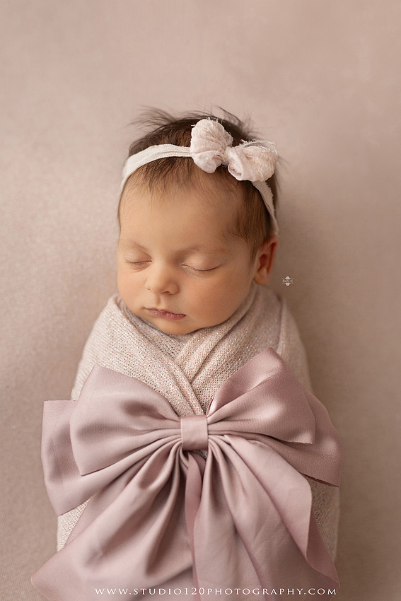 A collection of professional newborn portraits featuring a sleeping baby girl photographed in soft blush pink, ivory, and warm neutral tones. The gallery includes delicate floral headbands, a layered pink tutu, cozy cream wraps, a knitted lamb bonnet in a rustic wooden bucket, and beautiful cherry blossom accents. Images showcase a variety of classic newborn poses on textured blankets, nestled in a floral basket, and wrapped in timeless knit fabrics. Captured at Studio 120 Photography in Ramona, serving San Diego families with fine art newborn photography.