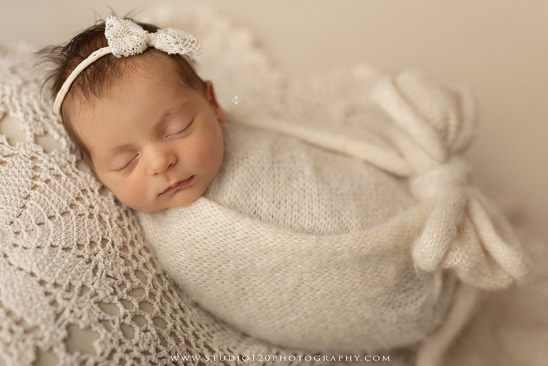 A collection of professional newborn portraits featuring a sleeping baby girl photographed in soft blush pink, ivory, and warm neutral tones. The gallery includes delicate floral headbands, a layered pink tutu, cozy cream wraps, a knitted lamb bonnet in a rustic wooden bucket, and beautiful cherry blossom accents. Images showcase a variety of classic newborn poses on textured blankets, nestled in a floral basket, and wrapped in timeless knit fabrics. Captured at Studio 120 Photography in Ramona, serving San Diego families with fine art newborn photography.