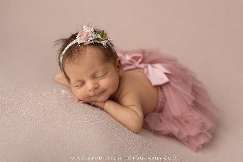 A collection of professional newborn portraits featuring a sleeping baby girl photographed in soft blush pink, ivory, and warm neutral tones. The gallery includes delicate floral headbands, a layered pink tutu, cozy cream wraps, a knitted lamb bonnet in a rustic wooden bucket, and beautiful cherry blossom accents. Images showcase a variety of classic newborn poses on textured blankets, nestled in a floral basket, and wrapped in timeless knit fabrics. Captured at Studio 120 Photography in Ramona, serving San Diego families with fine art newborn photography.