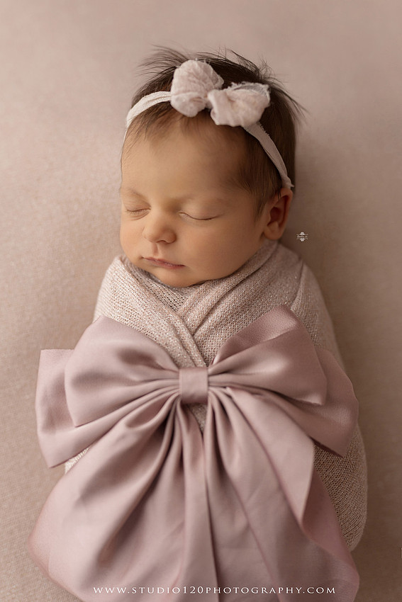A collection of professional newborn portraits featuring a sleeping baby girl photographed in soft blush pink, ivory, and warm neutral tones. The gallery includes delicate floral headbands, a layered pink tutu, cozy cream wraps, a knitted lamb bonnet in a rustic wooden bucket, and beautiful cherry blossom accents. Images showcase a variety of classic newborn poses on textured blankets, nestled in a floral basket, and wrapped in timeless knit fabrics. Captured at Studio 120 Photography in Ramona, serving San Diego families with fine art newborn photography.