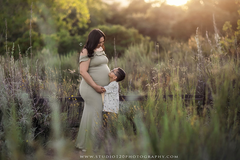 A golden hour maternity photography session at Lake Poway featuring an expecting family surrounded by wildflowers, rolling hills, and mountain views. The gallery includes romantic portraits of the parents, family photos with their young son, candid moments celebrating a growing family, and close-up images highlighting the mother's baby bump and the excitement of becoming a big brother. Captured in soft natural light with timeless neutral tones by Studio 120 Photography in Ramona, serving families throughout San Diego.