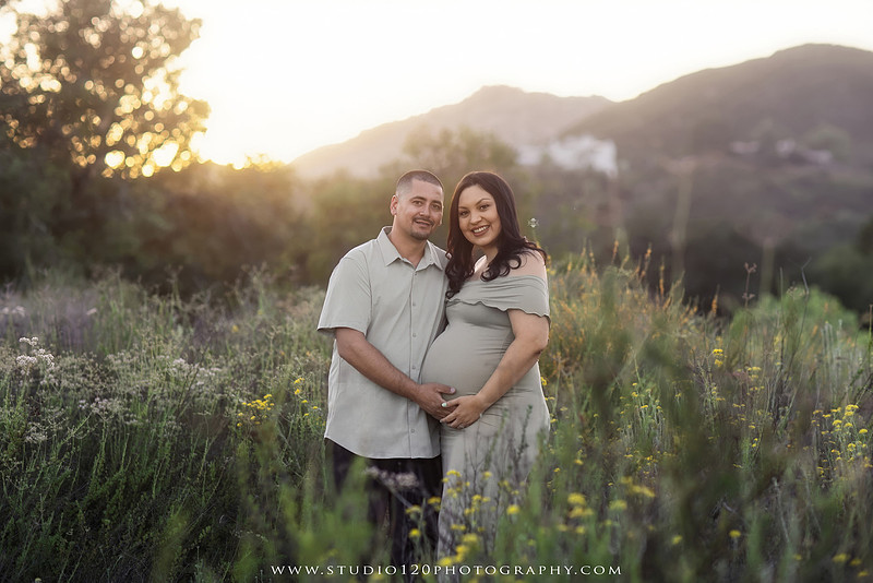 A golden hour maternity photography session at Lake Poway featuring an expecting family surrounded by wildflowers, rolling hills, and mountain views. The gallery includes romantic portraits of the parents, family photos with their young son, candid moments celebrating a growing family, and close-up images highlighting the mother's baby bump and the excitement of becoming a big brother. Captured in soft natural light with timeless neutral tones by Studio 120 Photography in Ramona, serving families throughout San Diego.