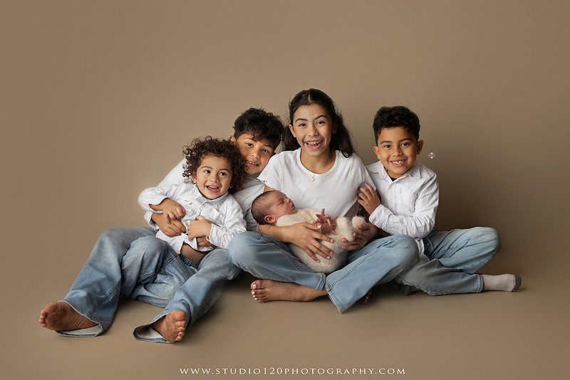 A professional newborn photography gallery featuring baby Caleb with his family at Studio 120 Photography in Ramona. The collection includes timeless family portraits with parents and four siblings, heartfelt individual parent and baby portraits, sibling photos gathered around a miniature crib, classic wrapped newborn poses, a personalized knit nightcap embroidered with Caleb's name, a custom football-themed newborn setup on a football under stadium lights, a football bowl prop with vintage football décor, and an organic newborn portrait with rich green knit textures and natural greenery. Soft neutral tones, personalized details, and family-centered images celebrate the arrival of a new baby while serving families throughout Ramona and the San Diego area.