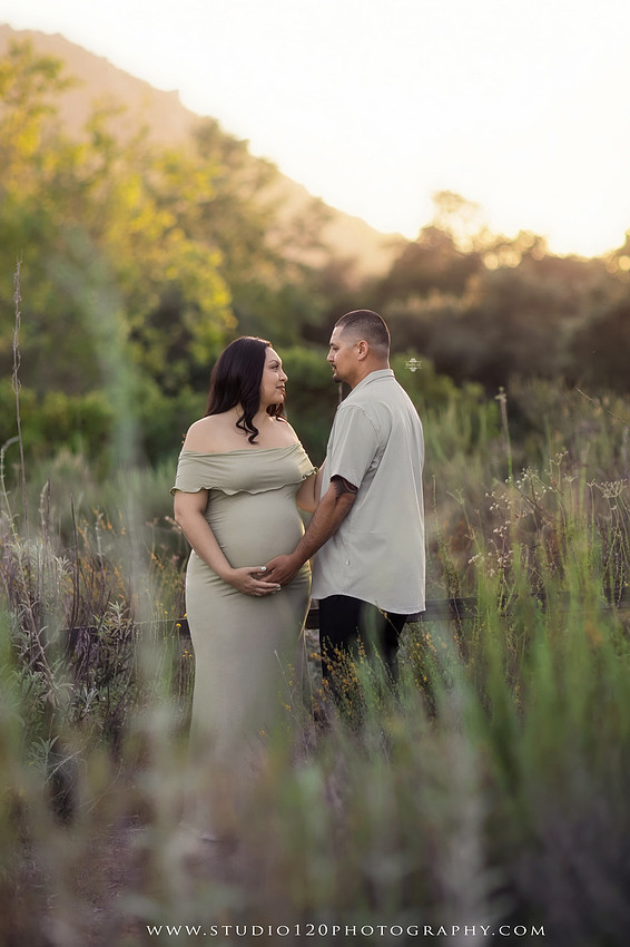 A golden hour maternity photography session at Lake Poway featuring an expecting family surrounded by wildflowers, rolling hills, and mountain views. The gallery includes romantic portraits of the parents, family photos with their young son, candid moments celebrating a growing family, and close-up images highlighting the mother's baby bump and the excitement of becoming a big brother. Captured in soft natural light with timeless neutral tones by Studio 120 Photography in Ramona, serving families throughout San Diego.