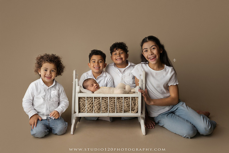 A professional newborn photography gallery featuring baby Caleb with his family at Studio 120 Photography in Ramona. The collection includes timeless family portraits with parents and four siblings, heartfelt individual parent and baby portraits, sibling photos gathered around a miniature crib, classic wrapped newborn poses, a personalized knit nightcap embroidered with Caleb's name, a custom football-themed newborn setup on a football under stadium lights, a football bowl prop with vintage football décor, and an organic newborn portrait with rich green knit textures and natural greenery. Soft neutral tones, personalized details, and family-centered images celebrate the arrival of a new baby while serving families throughout Ramona and the San Diego area.