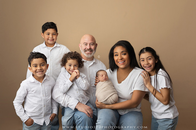 A professional newborn photography gallery featuring baby Caleb with his family at Studio 120 Photography in Ramona. The collection includes timeless family portraits with parents and four siblings, heartfelt individual parent and baby portraits, sibling photos gathered around a miniature crib, classic wrapped newborn poses, a personalized knit nightcap embroidered with Caleb's name, a custom football-themed newborn setup on a football under stadium lights, a football bowl prop with vintage football décor, and an organic newborn portrait with rich green knit textures and natural greenery. Soft neutral tones, personalized details, and family-centered images celebrate the arrival of a new baby while serving families throughout Ramona and the San Diego area.