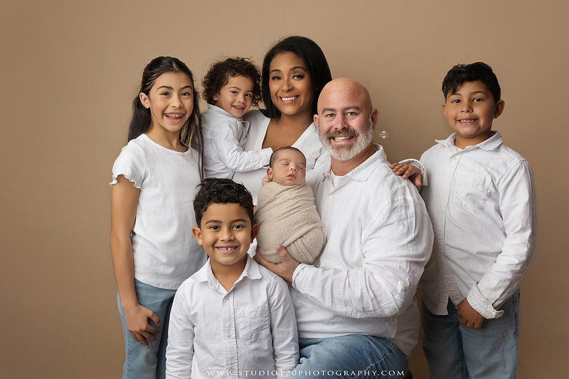 A professional newborn photography gallery featuring baby Caleb with his family at Studio 120 Photography in Ramona. The collection includes timeless family portraits with parents and four siblings, heartfelt individual parent and baby portraits, sibling photos gathered around a miniature crib, classic wrapped newborn poses, a personalized knit nightcap embroidered with Caleb's name, a custom football-themed newborn setup on a football under stadium lights, a football bowl prop with vintage football décor, and an organic newborn portrait with rich green knit textures and natural greenery. Soft neutral tones, personalized details, and family-centered images celebrate the arrival of a new baby while serving families throughout Ramona and the San Diego area.
