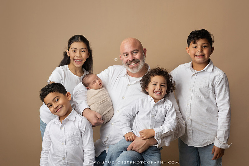 A professional newborn photography gallery featuring baby Caleb with his family at Studio 120 Photography in Ramona. The collection includes timeless family portraits with parents and four siblings, heartfelt individual parent and baby portraits, sibling photos gathered around a miniature crib, classic wrapped newborn poses, a personalized knit nightcap embroidered with Caleb's name, a custom football-themed newborn setup on a football under stadium lights, a football bowl prop with vintage football décor, and an organic newborn portrait with rich green knit textures and natural greenery. Soft neutral tones, personalized details, and family-centered images celebrate the arrival of a new baby while serving families throughout Ramona and the San Diego area.