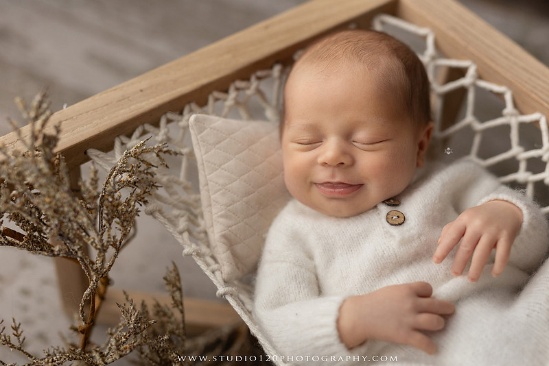 A collection of timeless newborn portraits featuring a sleeping baby boy photographed in Studio 120 Photography's Ramona studio. The gallery includes organic, neutral styling with soft cream wraps, textured knit blankets, rustic wooden bowls, vintage wash tubs, woven baskets, a modern macramé hammock, and a miniature woodland chair surrounded by handcrafted pine trees. Rich wood tones, eucalyptus greenery, dried botanicals, and warm natural textures create an elegant, earthy aesthetic. The collection also features simple beanbag portraits highlighting the baby's tiny features, peaceful sleeping poses, sweet smiles, and bright awake expressions. These fine art newborn photographs capture the beauty of a baby's earliest days with classic, heirloom-quality styling for families throughout Ramona, San Diego, Poway, Escondido, Lakeside, El Cajon, and surrounding Southern California communities.