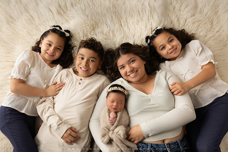 Timeless family newborn portraits featuring parents, siblings, and their new baby girl in soft neutral tones. The gallery includes standing family portraits, overhead sibling and newborn portraits, and natural moments celebrating the love, connection, and joy of welcoming a new baby. Captured at Studio 120 Photography in Ramona, serving San Diego County.