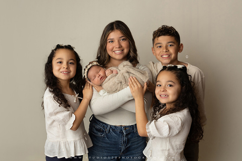 Timeless family newborn portraits featuring parents, siblings, and their new baby girl in soft neutral tones. The gallery includes standing family portraits, overhead sibling and newborn portraits, and natural moments celebrating the love, connection, and joy of welcoming a new baby. Captured at Studio 120 Photography in Ramona, serving San Diego County.