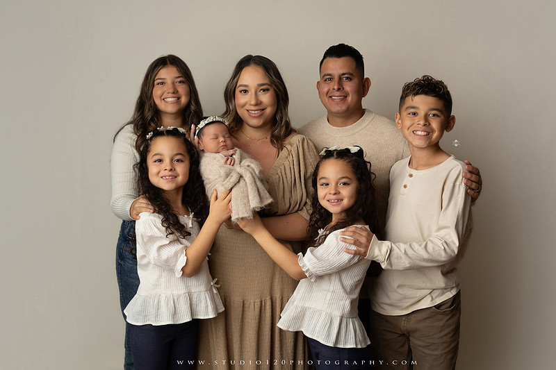 Timeless family newborn portraits featuring parents, siblings, and their new baby girl in soft neutral tones. The gallery includes standing family portraits, overhead sibling and newborn portraits, and natural moments celebrating the love, connection, and joy of welcoming a new baby. Captured at Studio 120 Photography in Ramona, serving San Diego County.
