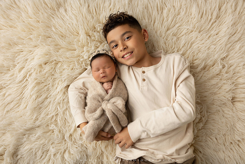 Timeless family newborn portraits featuring parents, siblings, and their new baby girl in soft neutral tones. The gallery includes standing family portraits, overhead sibling and newborn portraits, and natural moments celebrating the love, connection, and joy of welcoming a new baby. Captured at Studio 120 Photography in Ramona, serving San Diego County.