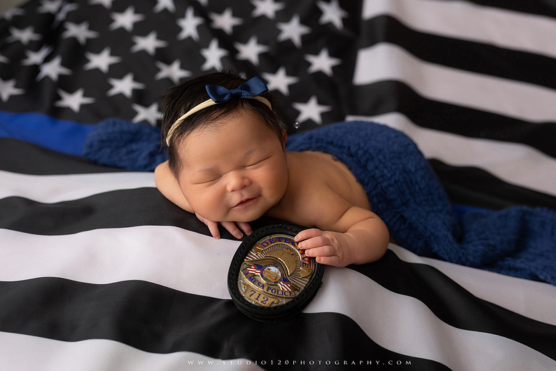 A collection of newborn baby girl portraits featuring peaceful sleeping poses, soft neutral wraps, delicate floral headbands, textured blankets, rustic baskets, natural wood props, creamy backdrops, and a special police tribute setup with a badge and Thin Blue Line flag. The gallery showcases timeless, baby-led newborn photography with warm, organic tones at Studio 120 Photography in Ramona, serving San Diego County.