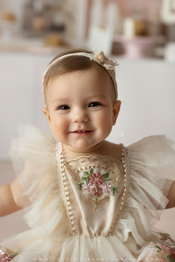 One Tough Cookie first birthday cake smash photography session featuring a baby girl in a soft pink bakery-themed set, chef outfit, floral dress, cookies, birthday cake and cake smash portraits at Studio 120 Photography in Ramona, California.