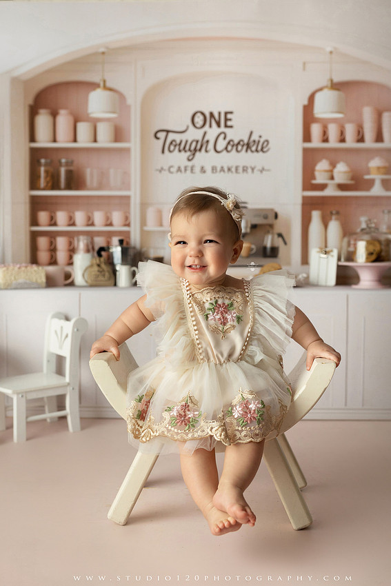 One Tough Cookie first birthday cake smash photography session featuring a baby girl in a soft pink bakery-themed set, chef outfit, floral dress, cookies, birthday cake and cake smash portraits at Studio 120 Photography in Ramona, California.